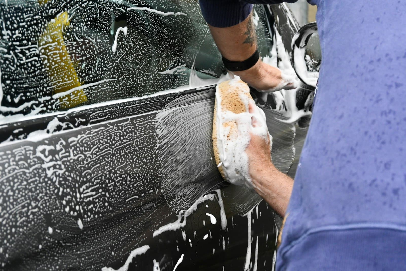 Close-up of a car door being hand washed with a soapy sponge